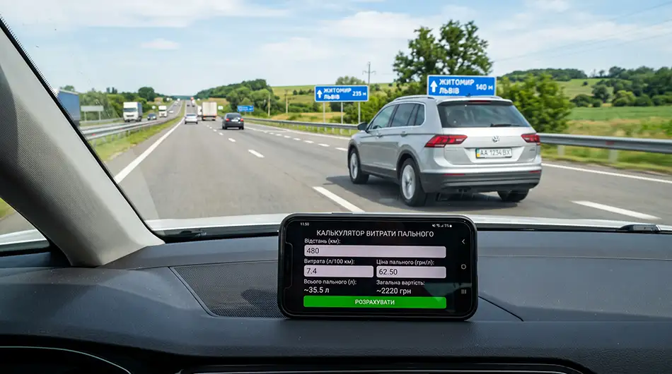 сучасний легковий автомобіль на трасі, на передньому плані смартфон з екраном онлайн-калькулятора витрати пального, поруч умовні дані «480 км», «7,4 л/100 км», «62,50 грн/л»